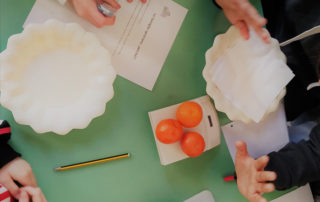Un banco con due piatti e mandarini al centro mentre tre bambini sono seduti attorno