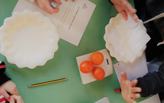 Un banco con due piatti e mandarini al centro mentre tre bambini sono seduti attorno
